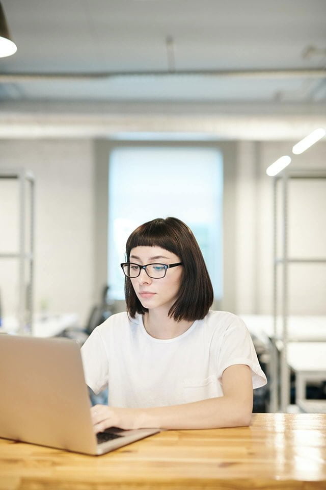 Ragazza con gli occhiali che lavora al computer portatile in ufficio